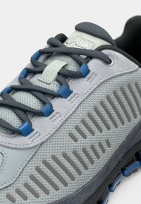 Grå atletisk joggesko med mesh-overdel med teksturdetaljer, blå lisser og gummisåle med horisontale riller.