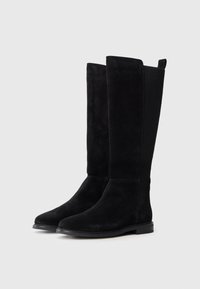 Bottes en suede noir jusqu'aux genoux avec une texture lisse, un bout effilé et des panneaux latéraux élastiques. Elles sont dotées d'une semelle en caoutchouc plate pour plus de stabilité.