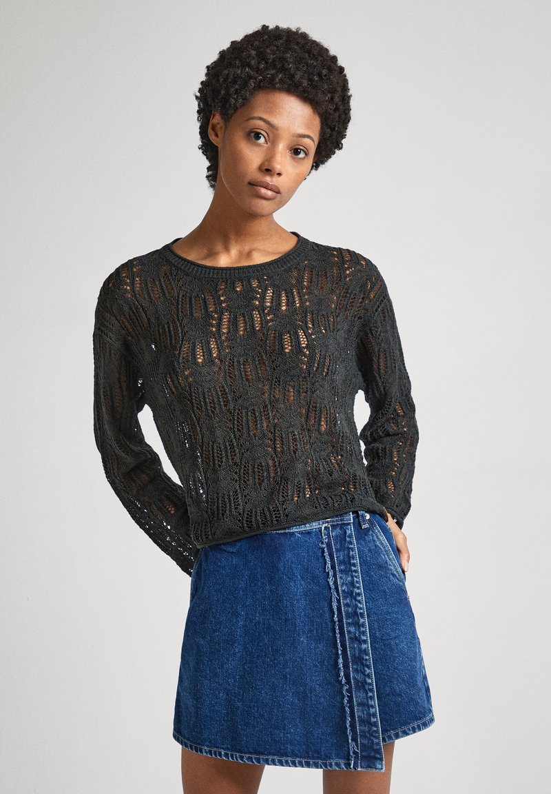 Svart stickad tröja med ett texturerat, öppet spetsmönster och långa ärmar, kombinerad med en blå denimkjol med franskant.