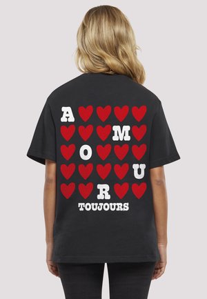 Tricou negru din bumbac, cu litere albe și roșii îndrăznețe și grafică cu inimioare pe spate, având textul „AMOUR TOUJOURS.”