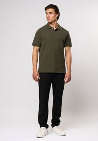 Oliven grønn bomull polo skjorte med krage og korte ermer, kombinert med svarte tapered bukser og hvite joggesko. Enkel design med brodert logo.