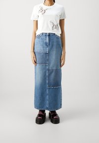 Bílé tričko s krajkovou aplikací motýla, sladěné s maxi sukní z džínoviny s patchworkem. Černé platformové boty s lesklým povrchem.