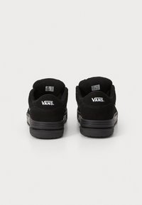 Paire de baskets Vans noires vues de dos, avec le logo Vans blanc sur le talon et des semelles en caoutchouc noir texturé.