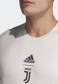 Witte katoenen T-shirt met het zwarte Adidas-logo en het Juventus-insigne. Voorzien van een ronde hals en korte mouwen, met een gladde textuur.