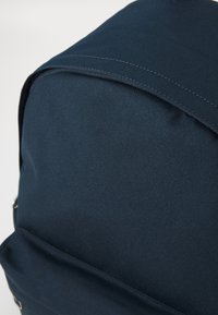 Mörkblå tygryggsäck med en slät yta, rundad topp, synlig sömnad och en elegant design. Har en frontficka och dragkedjor.