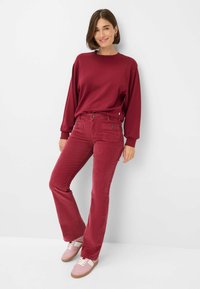 Bordeaux sweatshirt met lange mouwen, gecombineerd met bijpassende bordeaux corduroy flared pants met voorkeuzes en knoopaccenten. Lichte roze sneakers.
