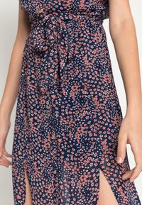 Abito floreale con sfondo navy, decorato con fiori rosa e bianchi, con vita legata e spacchi laterali, realizzato in tessuto leggero.
