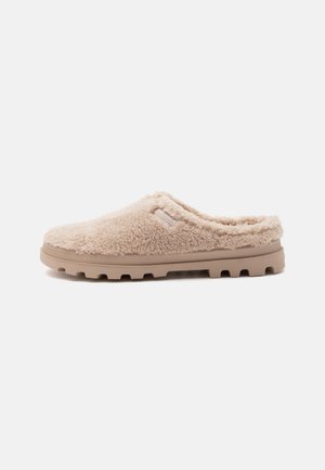 Chausson beige à enfiler avec une texture duveteuse, semelle en caoutchouc avec relief et un talon bas pour un enfilage facile.