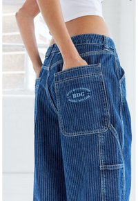 Cargo jeans i mörkblått med vertikala vita ränder. Har flera fickor, förstärkta sömmar och en synlig logotyp på fickan.