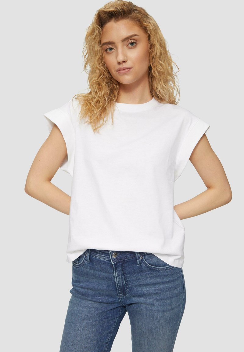 Witte katoenen T-shirt met opgerolde korte mouwen, ronde halslijn, relaxte pasvorm, gedragen met blauwe spijkerbroek. Eenvoudig en veelzijdig ontwerp.