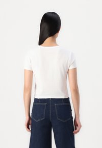Biely krátky tričko s krátkymi rukávmi, okrúhlym výstrihom, vyrobené z jemnej bavlny; v kombinácii s nohavicami z tmavého denimu s vysokým pásom, ktoré majú zadné vrecká.