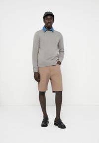 Hellgrauer Pullover, blaues Hemd mit Kragen, beiges Shorts und schwarze Slipper. Einfaches Design, neutrale Farben und taillierte Passform.