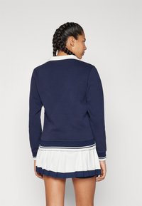 Marinblå sweatshirt med vit krage och ribbade muddar, tillsammans med en vit plisserad kjol med marinblå kant vid fållen.