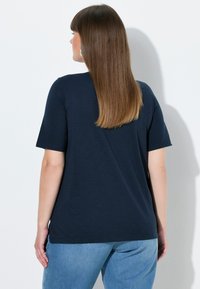 Mørkeblå T-shirt med korte ærmer lavet af blødt stof. Har et afslappet snit med en lidt længere bageste kant og sidesplitter.