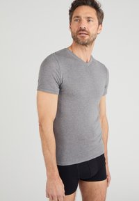 T-shirt grigio a maniche corte con scollatura a V realizzato in tessuto morbido, design aderente, abbinato a boxer neri, in piedi su uno sfondo neutro.