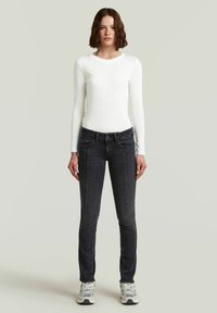 Witte lange mouwen top en donkergrijze skinny jeans, met een gladde textuur en een fitted ontwerp. G gedragen met grijze en witte sneakers.