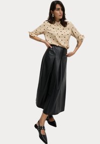 Beige kortärmad skjorta med svarta prickar, ihopparad med en svart veckad läderskirt och svarta spetsiga ballerinas med dekorativa detaljer.