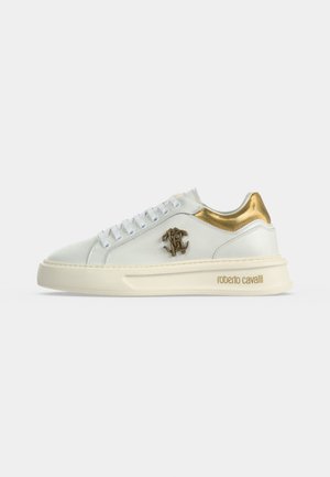 Άσπρο sneaker χαμηλού άξονα με χρυσή λεπτομέρεια στη φτέρνα, μεταλλικό λογότυπο στο πλάι, παχύ κρεμώδες πέλμα και "roberto cavalli" ανάγλυφο κοντά στη φτέρνα.