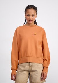 Orangecoloret sweatshirt i bomuld med ribbede halsudskæring og manchetter, med et lille broderet logo på venstre bryst. Sammen med beige shorts.