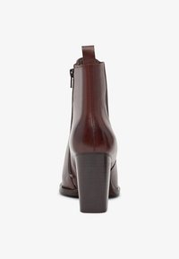 Botte en cuir marron de cheville avec un talon épais, fermeture à glissière sur le côté et un détail de couture subtil à l'arrière. texture lisse, design épuré.