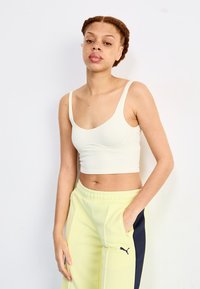 Light beige ribbed crop top with thin straps, paired with yellow sweatpants featuring a black side stripe and logo.