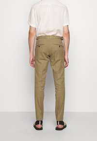 Světlé khaki kalhoty vyrobené z texturované látky, s dvěma zadními kapsami na knoflíky, zúženými nohavicemi a středním pasem.