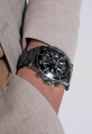 Sort chronograf ur med stållederstrop, der har en sort urskive, sølv accenter og tre små urskiver til tidsmåling.