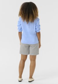 Világoskék ing felgöngyölt ujjakkal, fekete-fehér csíkozott nadrággal párosítva, hátulról nézve. Simát tapintás; casual dizájn.