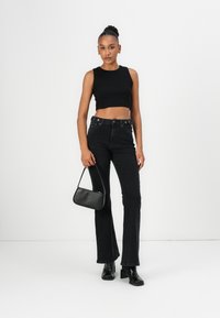 Black cropped tank top paired with high-waisted black flared jeans. Model holds a small black handbag, featuring a smooth texture and simple design.