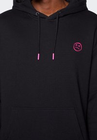 Svart hoodie med framficka, försedd med en rosa broderad smiley och färgmatchade snoddtips. Mjuk tygkänsla och avslappnad passform.
