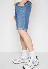 Shorts de mezclilla en azul claro con un corte regular, dobladillos enrollados y diseño de cinco bolsillos. Combinados con zapatillas deportivas blancas y plateadas y calcetines.