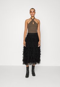 Brown halter top with a keyhole detail and a black, tiered ruffled tulle skirt. Finished with ankle-length black boots.