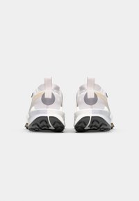 Sportliche Schuhe mit einem weißen Mesh-Obermaterial, beigen und grauen Akzenten sowie einer robusten schwarzen Außensohle mit strukturiertem Grip. Zwei Zugschlaufen an der Ferse.