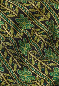 Tekstiili, millel on must taust, millel on keerukad rohelised lillemustrid ja kuldsed aktsendid. Pehme tekstuur nähtavate kootud detailidega.