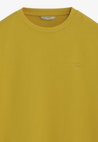 T-shirt jaune à col rond en coton, avec une broderie discrète "Scalpers Company" sur le devant. Texture lisse et légère.