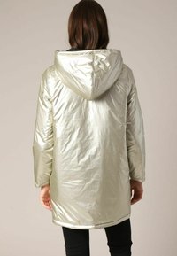 Parka à capuche argent métallique, dotée d'une texture lisse et brillante, au design longueur genou, avec des poches avant pour une fonctionnalité accrue.