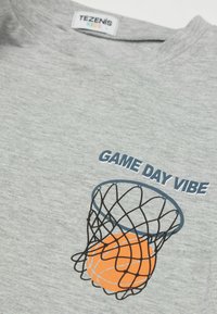Šedé tričko s krátkým rukávem s modro-černou grafikou basketbalového koše, oranžovým basketbalem a textem "GAME DAY VIBE" vytištěným na přední straně.