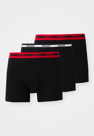 Ensemble de boxeurs noirs, trois pièces. Comprend des ceintures élastiques rouges et blanches avec le logo "HUGO". Tissu doux, design ajusté, jambe mi-longue.