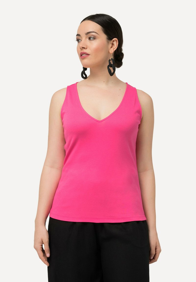 Top in cotone rosa con scollatura a V. Il top presenta una vestibilità slim ed è abbinato a pantaloni neri a gamba larga.