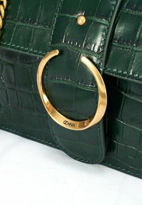 Zielona torebka skórzana tłoczona w wzór krokodyla z okrąłym złotym zdobieniem oraz detalami przeszyć. Kompaktowy design o gładkiej fakturze.