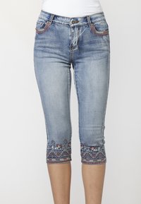 Light blue cropped denim jeans with embroidered hems and pocket trim, worn with a white top, against a plain white background.