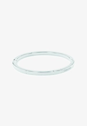 Srebrna kovinska zapestnica brez spojnic z gladko površino. Ima minimalističen dizajn in diskretno gravuro logotipa Calvin Klein.