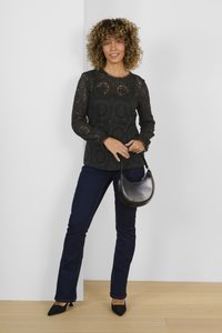 Top in pizzo nero con maniche lunghe, motivo floreale, abbinato a jeans scuri e scarpe con tacco nere, mentre tiene una piccola borsa nera a tracolla.