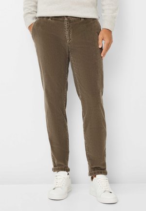 Pantalon en velours côtelé brun avec une coupe ajustée et une texture à côtes verticales. Porté avec des baskets blanches, présentant un design décontracté et relax.