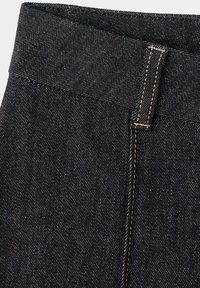 Gros plan sur un tissu en jean foncé montrant la ceinture, la boucle de ceinture et une double couture avec un fil contrastant.