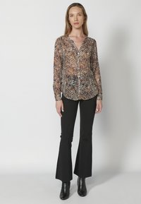 Camicia a maniche lunghe con motivo di foglie multicolore, realizzata in tessuto leggero. Abbinata a pantaloni neri a zampa d'elefante e stivali neri con tacco.