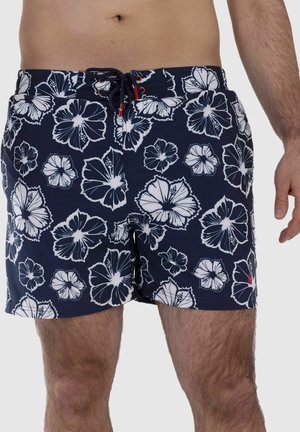 Male torso and legs wearing navy blue swim shorts with white hibiscus flower print and black drawstring tie at the waist.