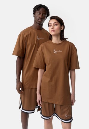 Brown cotton t-shirts with short sleeves and oversized fit, featuring white logo. Paired with brown shorts with black and white accents.
