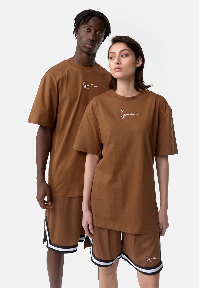 Brown cotton t-shirts with short sleeves and oversized fit, featuring white logo. Paired with brown shorts with black and white accents.