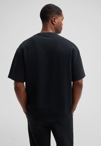 Zwarte oversized katoenen T-shirt met een ronde halslijn, korte mouwen en een gladde textuur, gezien vanuit de achterkant.